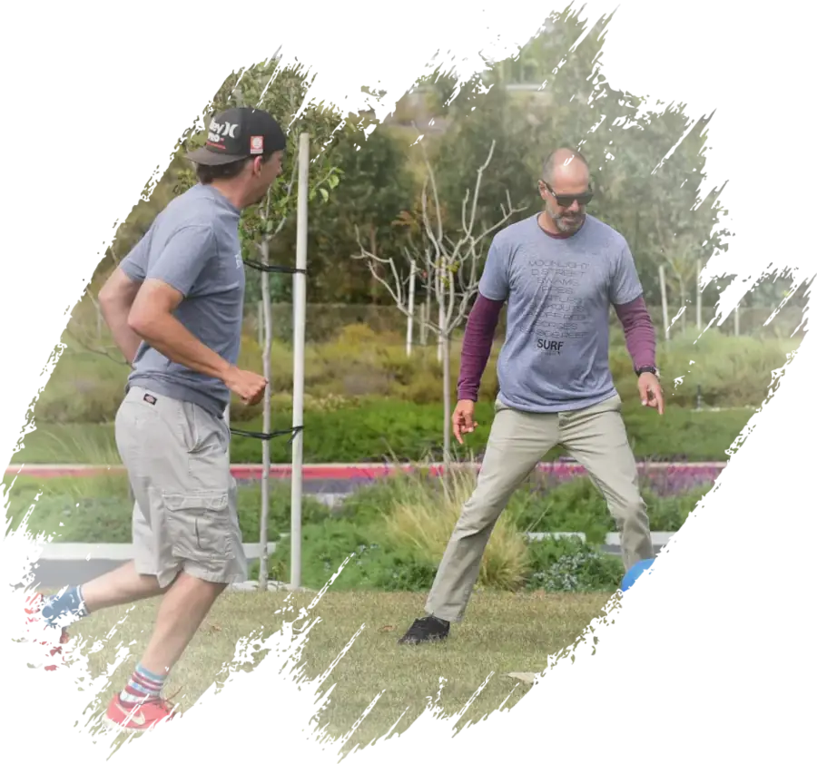 John participating in an outdoor fitness session on a lawn, facing another man who is jogging in place.