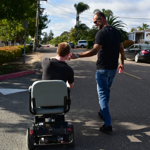 John fist-bumping a man riding a motorized mobility scooter down a residential street.