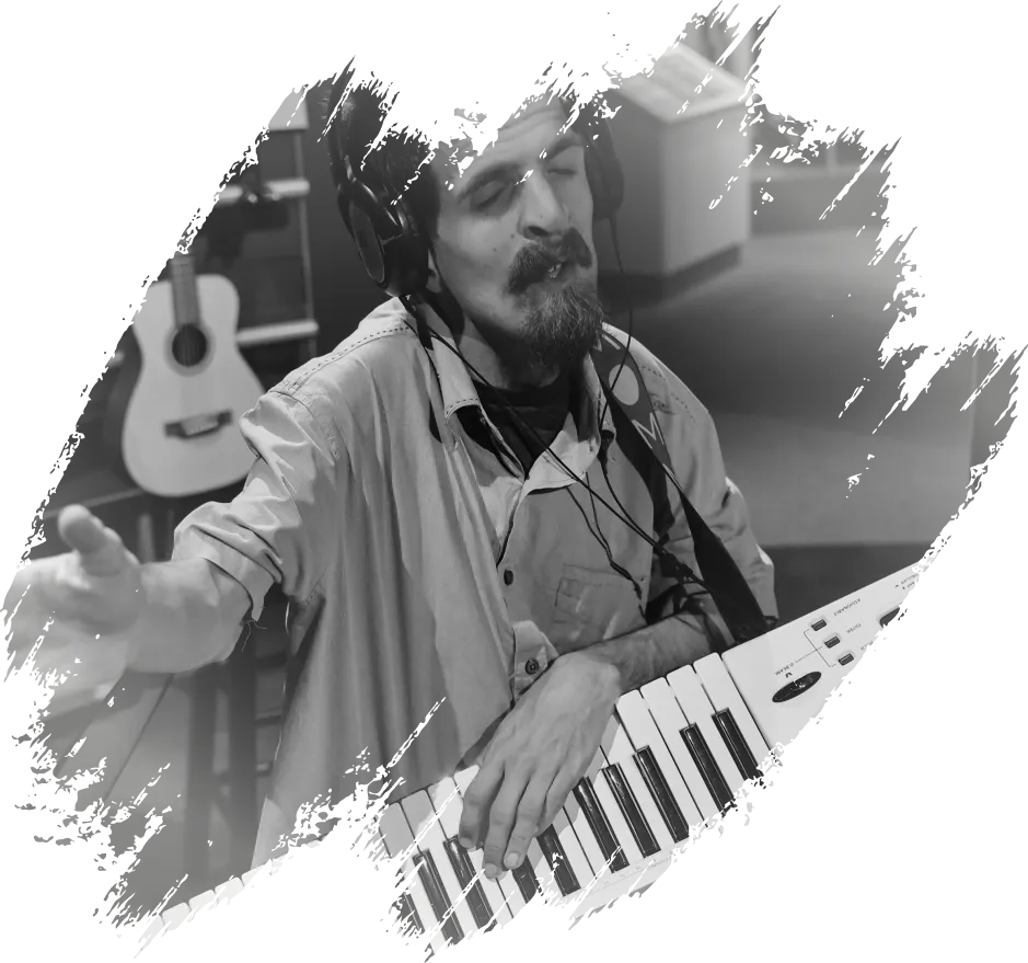 A man wearing headphones, singing with his eyes closed while playing a keytar with his hand extended forward.