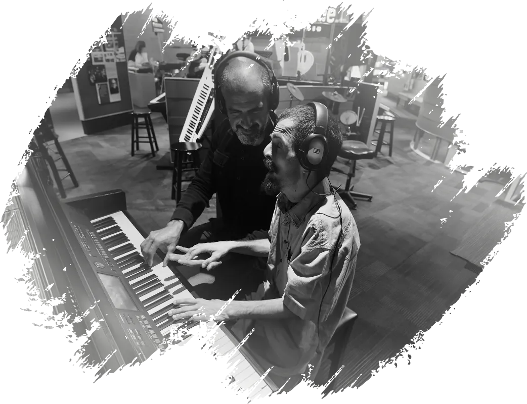 John wearing headphones and guiding a student's hands on a piano keyboard.