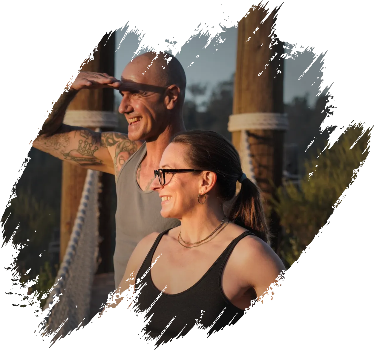 The Founders John and Christina smiling and looking into the distance while standing on a wooden bridge during sunset.